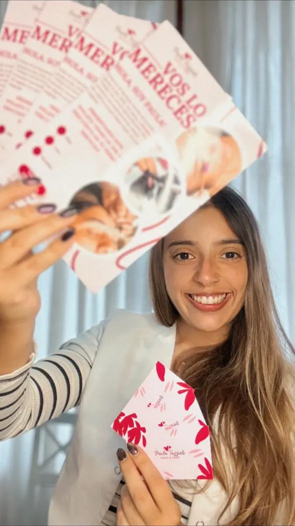 Paula sonriendo mientras muestra folletos y una tarjeta de su marca